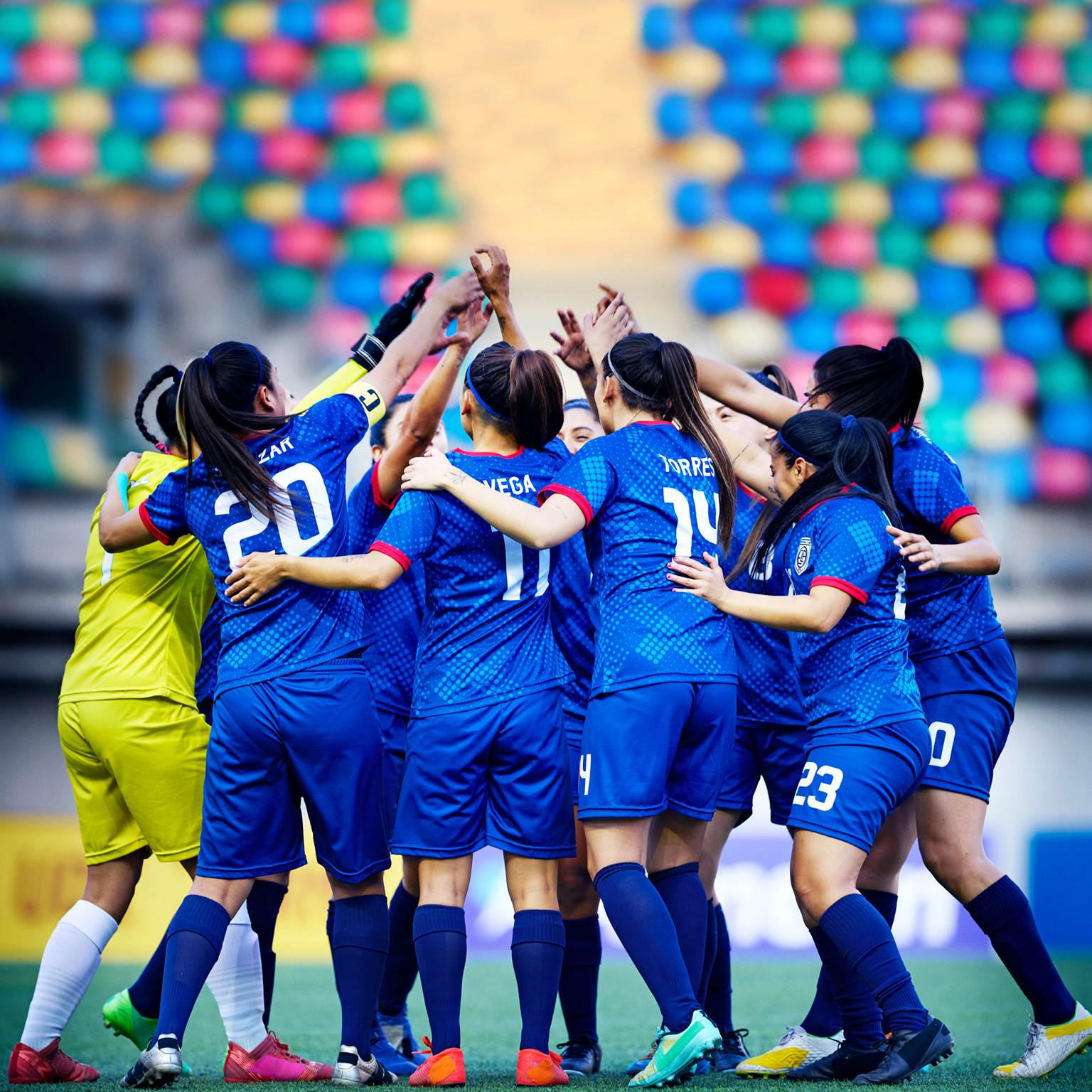 A professional women's soccer team forms a circle with their arms raised and embracing.