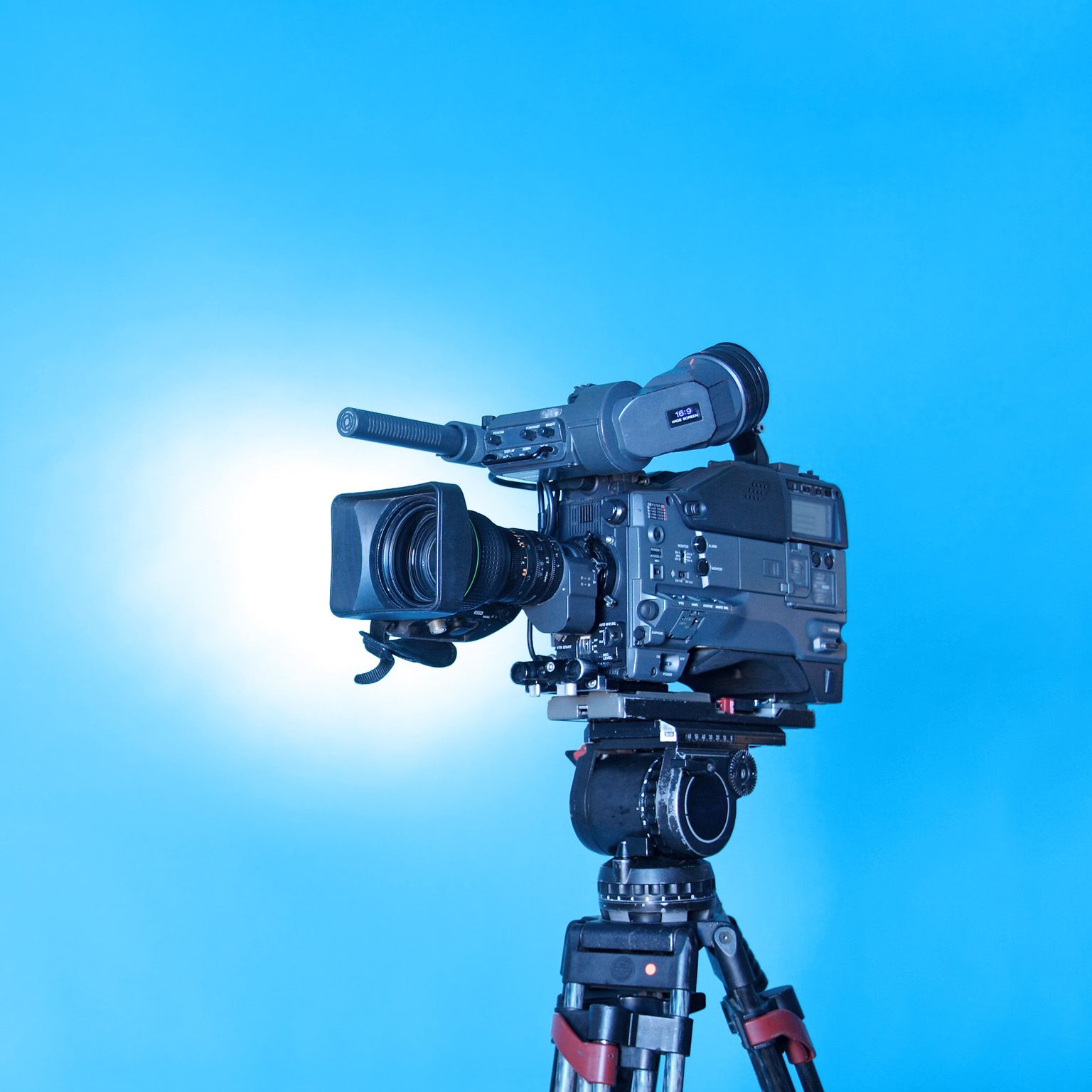 A professional video camera on a tripod with a rich gradient blue background.