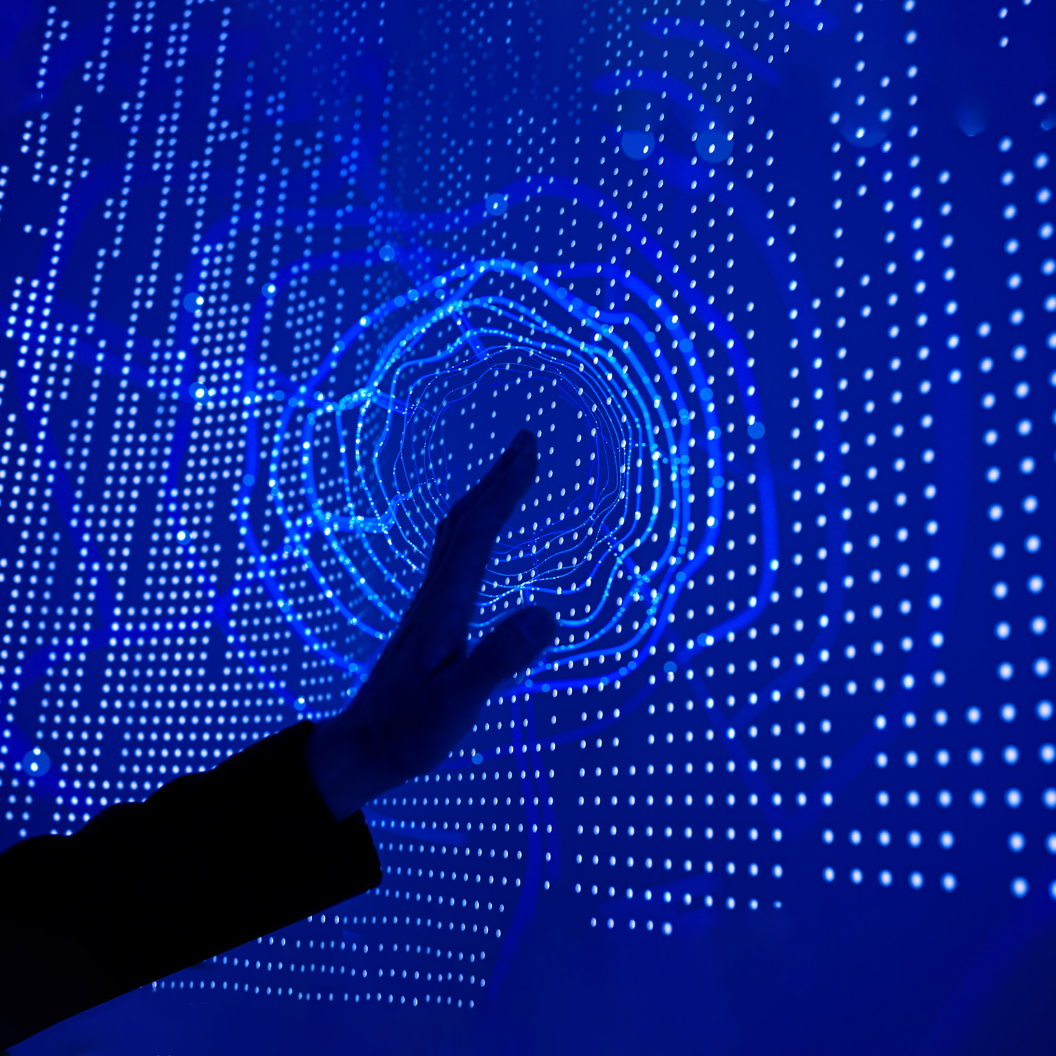 A hand reaching out to touch a deep blue screen covered in datapoint dots. A circular ripple effect emanates from the point of contact.