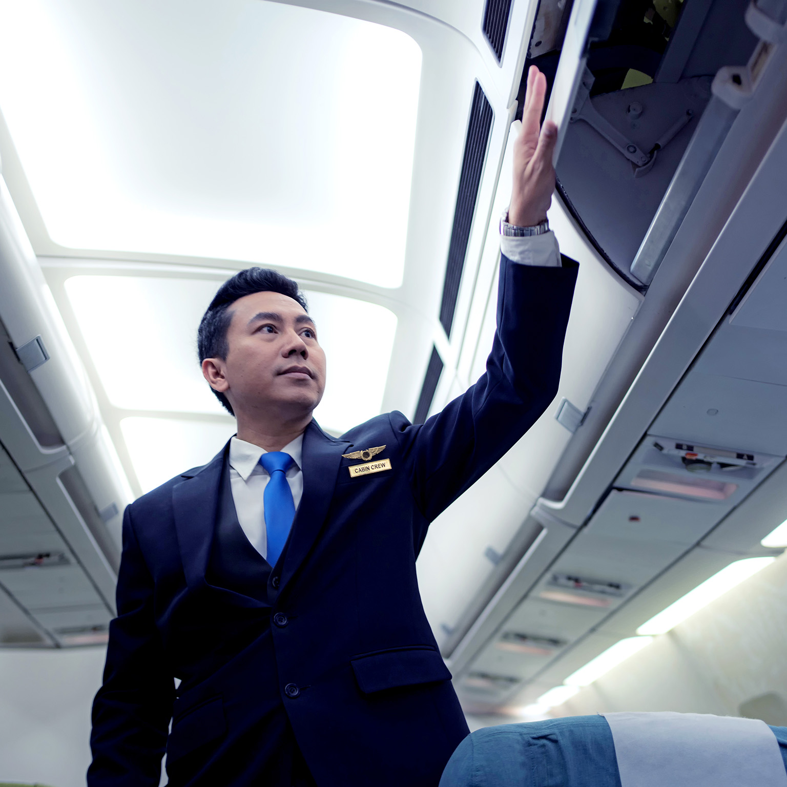 Image of a flight attendant closing overhead bins on an empty plane.