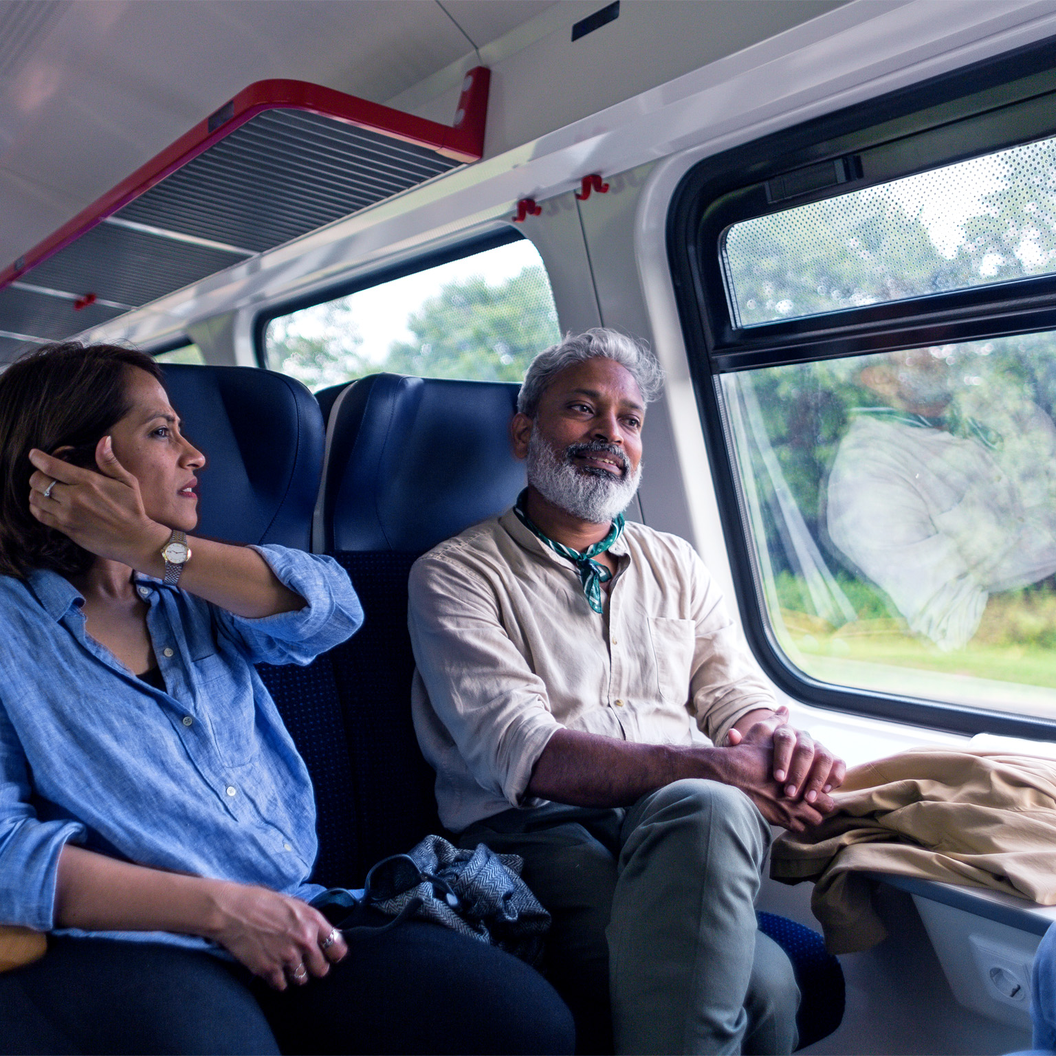 A mature Indian tourist couple riding in a commuter train in Lithuania, talking, having fun, and looking out the window.