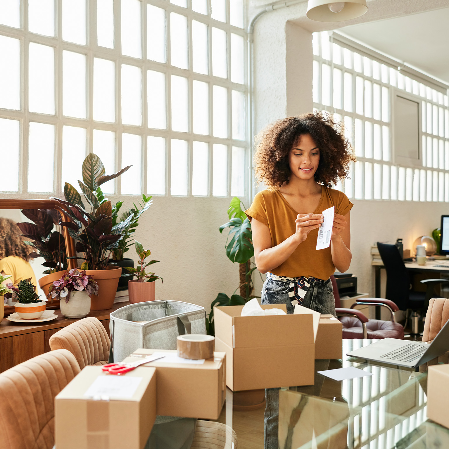 Confident businesswoman holding sticky bill. Young female entrepreneur is working at home office. Packages are on table.