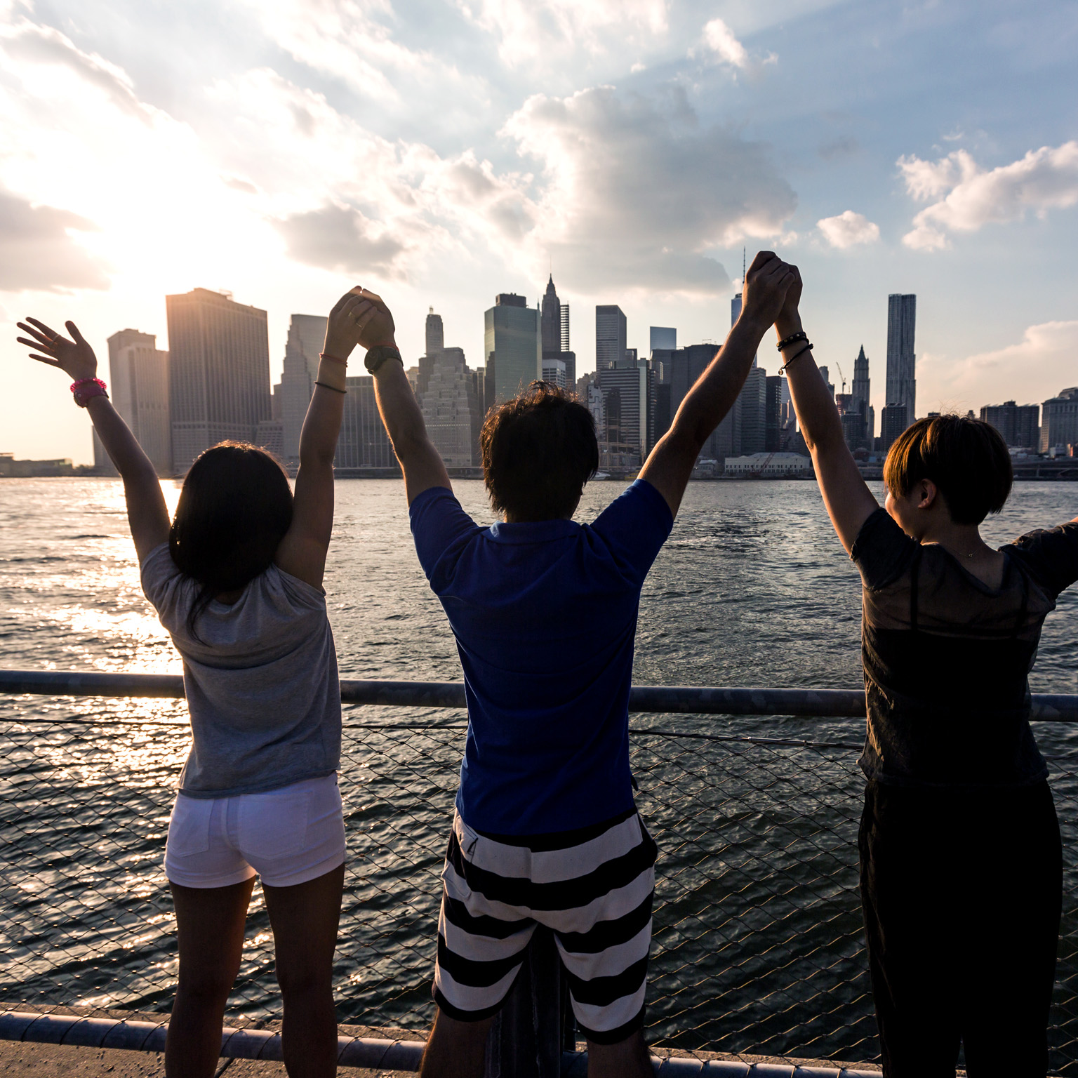 Three friends holding hands in celebration across the water from a city skyline