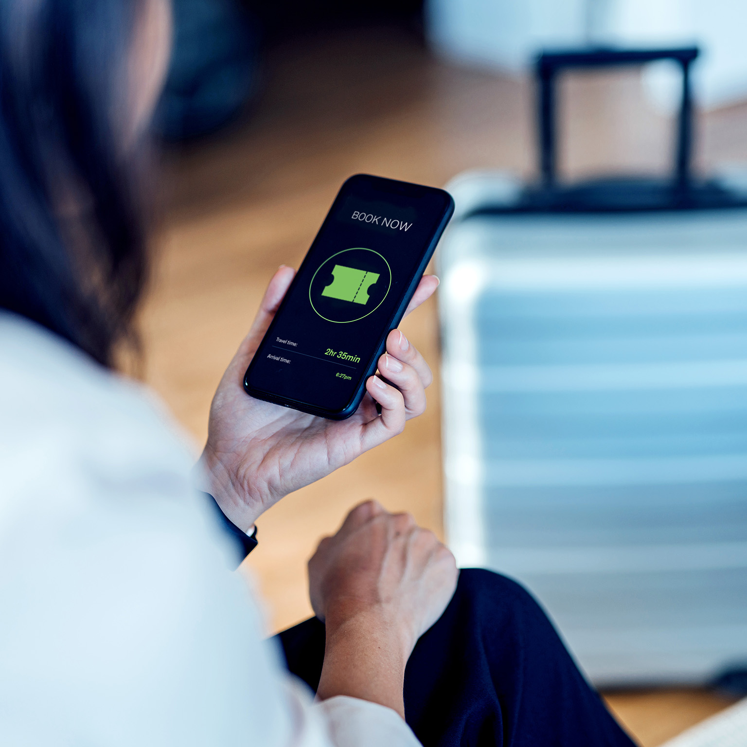 Image of a person purchasing a ticket on a mobile device with a suitcase in the background.