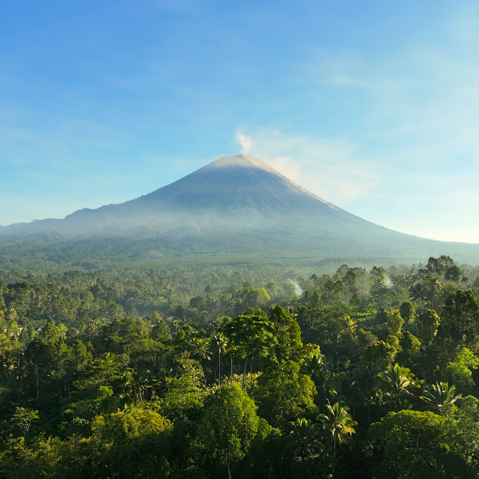 Scenic aerial view sunrise scene of Tumpak Sewu waterfall with Semeru Volcano Background with the jungles on Java Island, Indonesia.