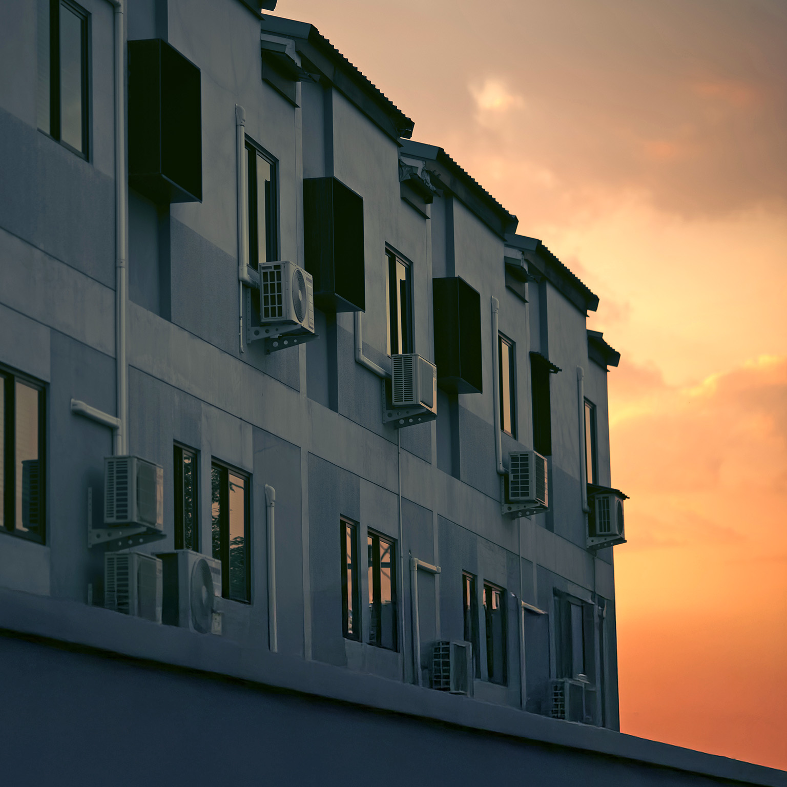 Image of an apartment building with air conditioning units next to the windows bathed in golden sunset.