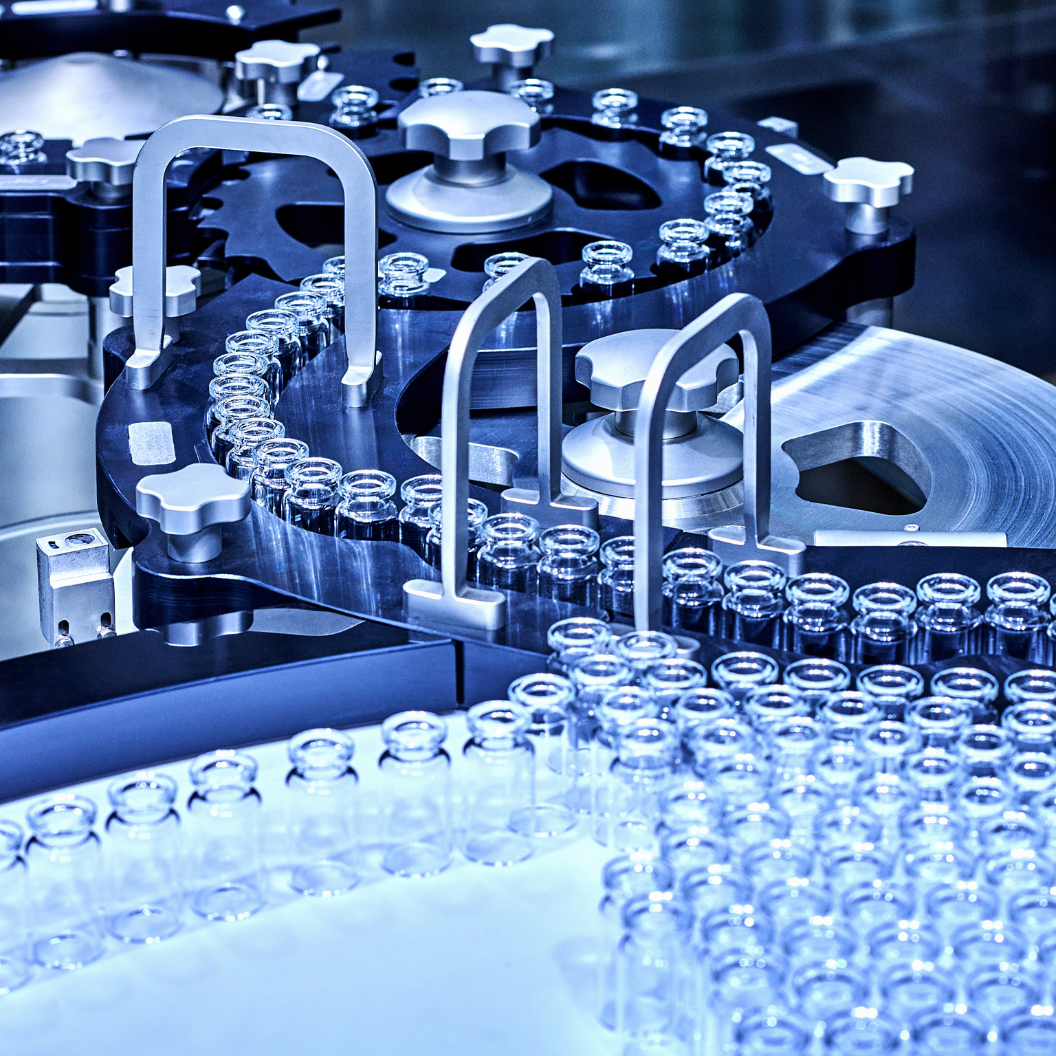 A pharmaceutical production line with rows of small glass vials moving through a complex stainless-steel machine.