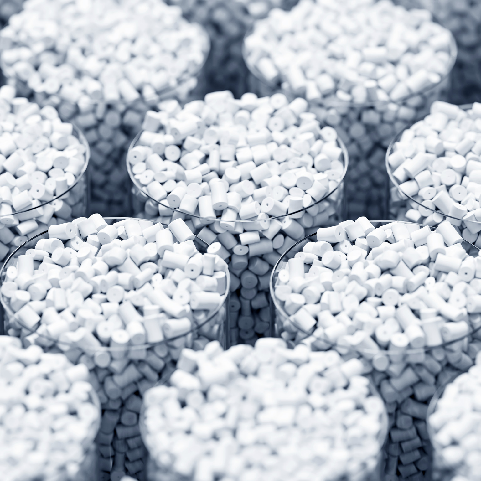 Multiple transparent containers filled with small white cylindrical plastic pellets arranged in a repeating pattern.
