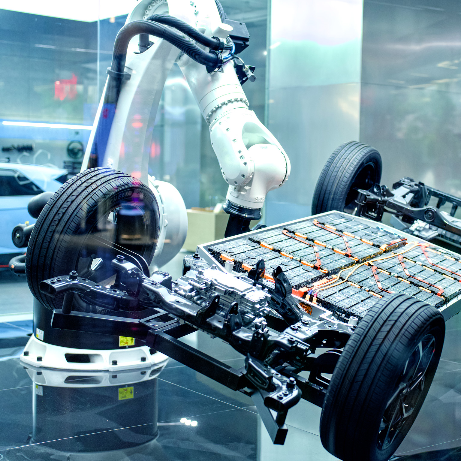 The exposed chassis and battery platform of an electric vehicle surrounded by robotic arms in a high-tech manufacturing or display environment.