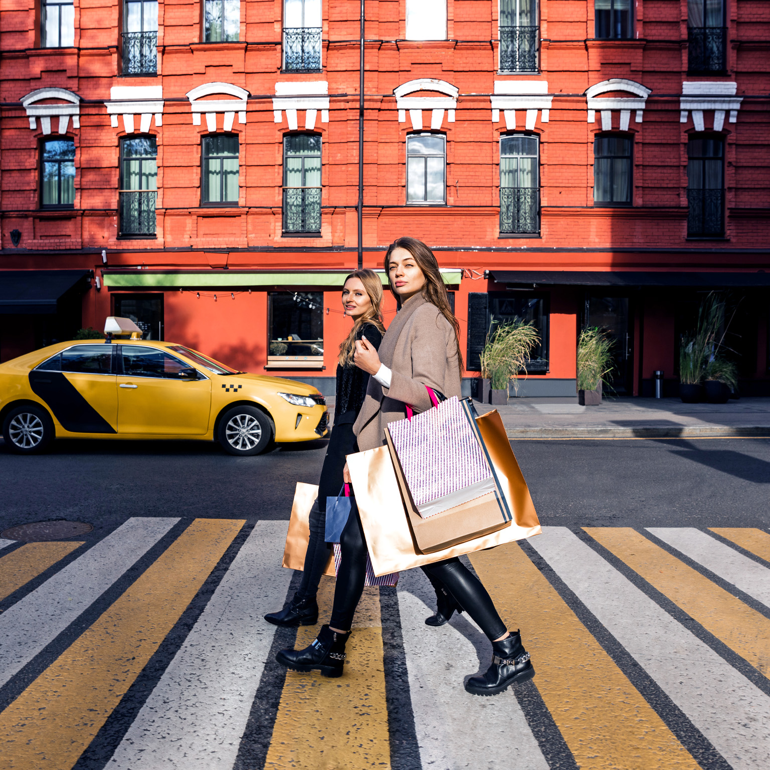 Two women with shopping bags walking across a street crosswalk
