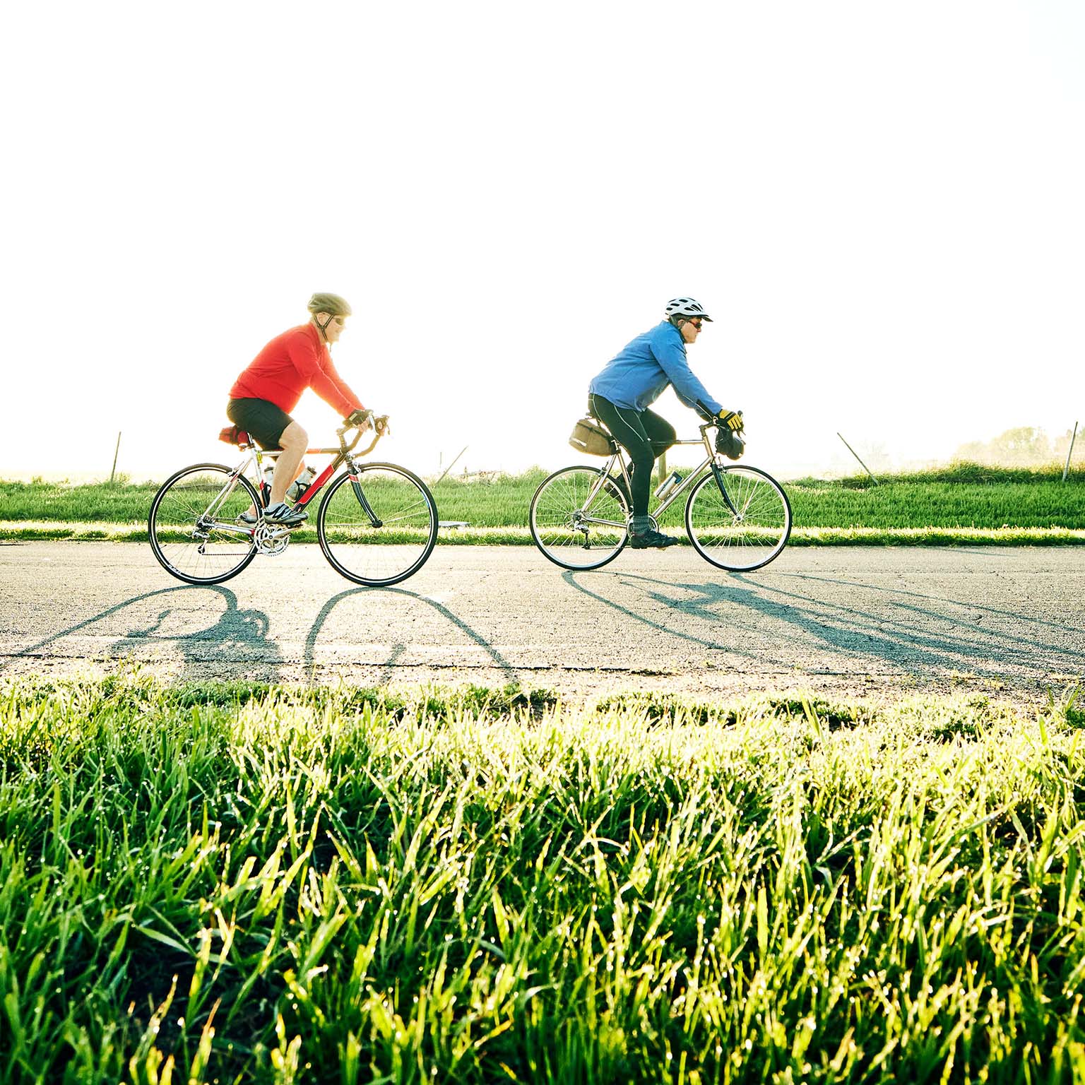 Wide shot of senior male friends on sunrise bike ride on rural road