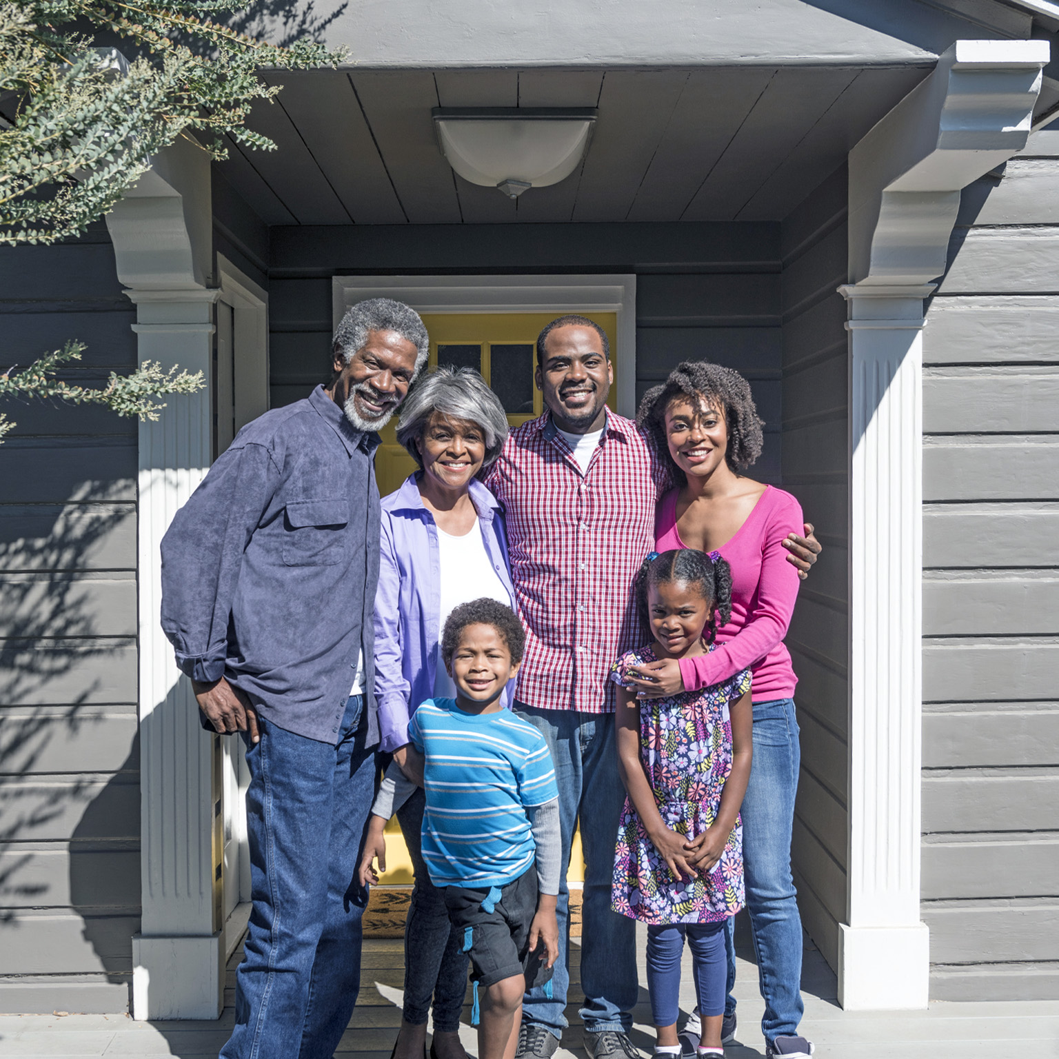 Three generations of a Black family pose together and smile outside their home.