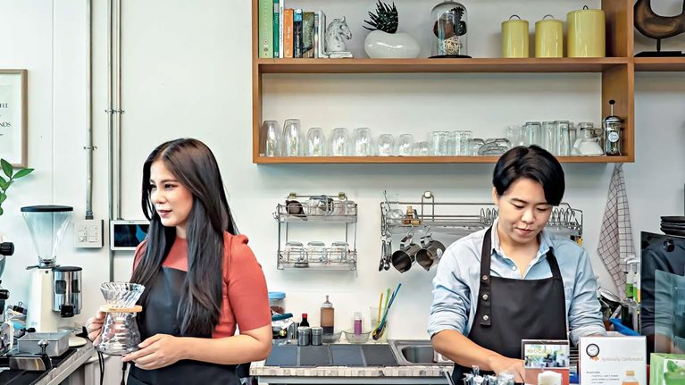 Two employees operating a modern café with professional coffee equipment and organized workspace
