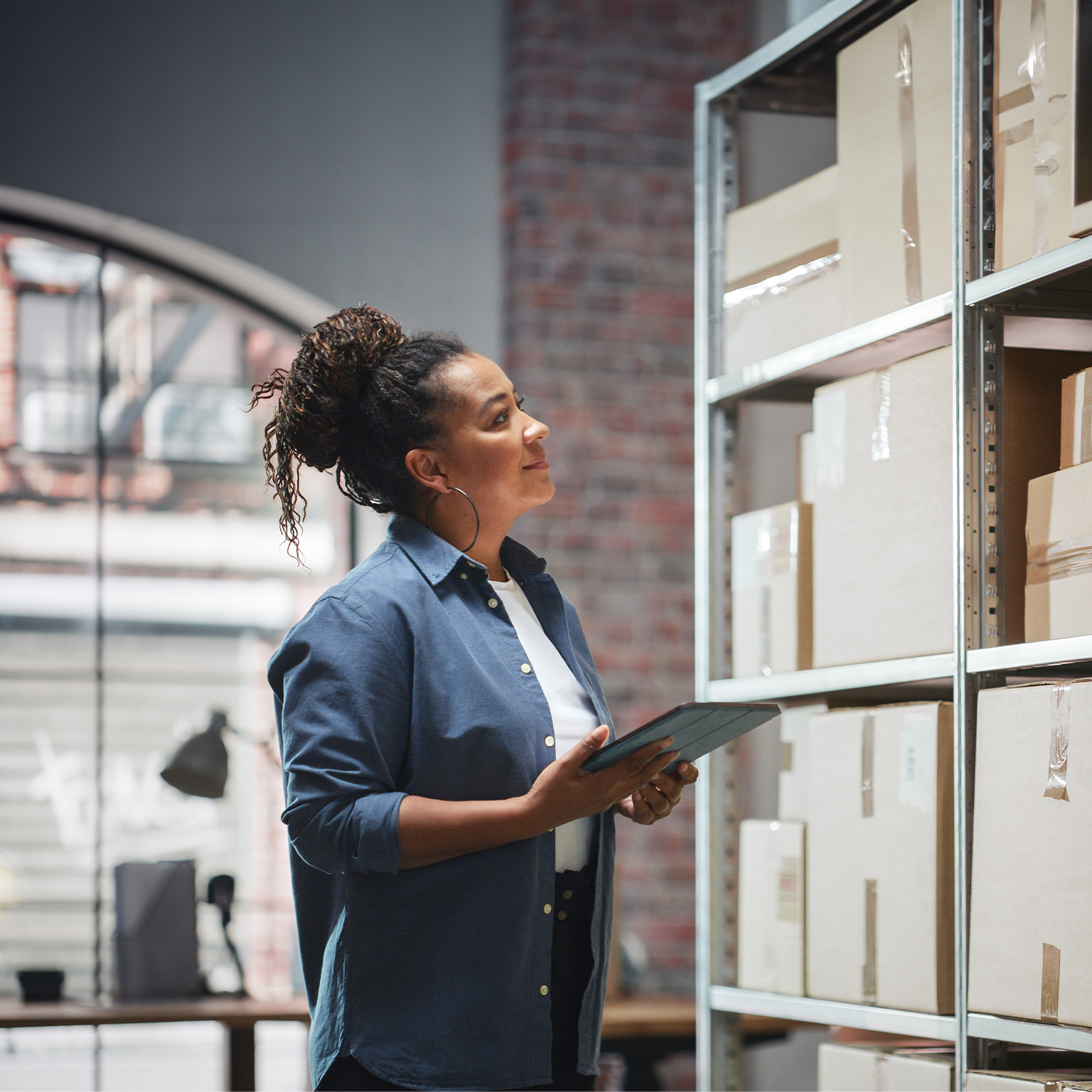 Portrait of a Manager Checking Inventory, Writing in Tablet Computer. Black Woman Working in a Warehouse Storeroom with Rows of Shelves Full of Parcels, Packages with Orders Ready for Shipment. - stock photo