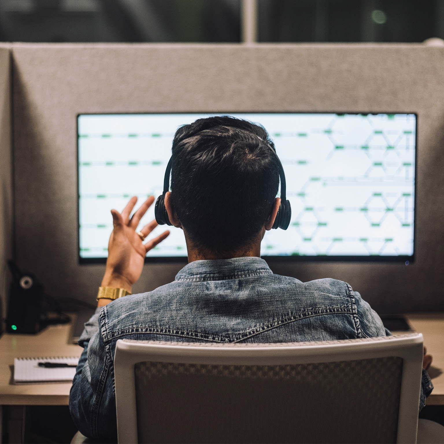 Rear view of young male customer service executive talking through headset sitting at desk in illuminated call center