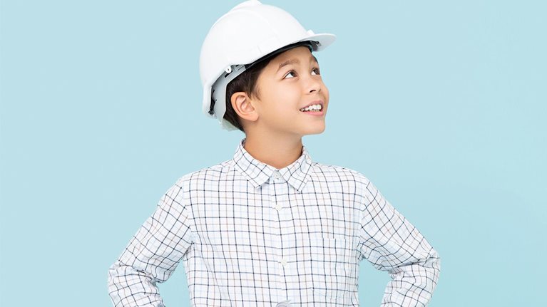 Smiling young boy aspiring to be future engineer wearing white hard hat and holding blueprint - stock photo