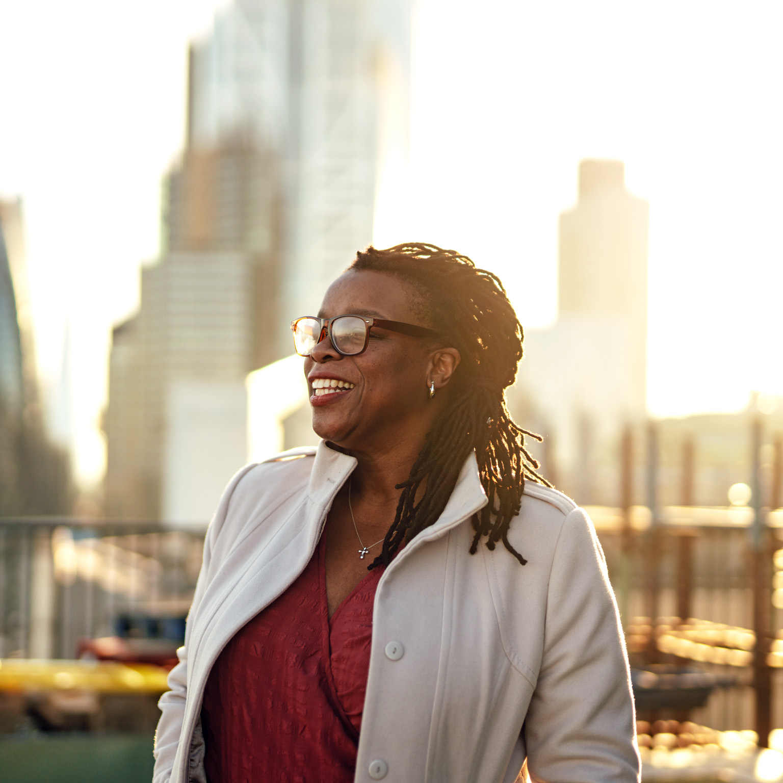 A mature businesswoman standing with her hands in pockets on office building rooftop with the London cityscape in the background.