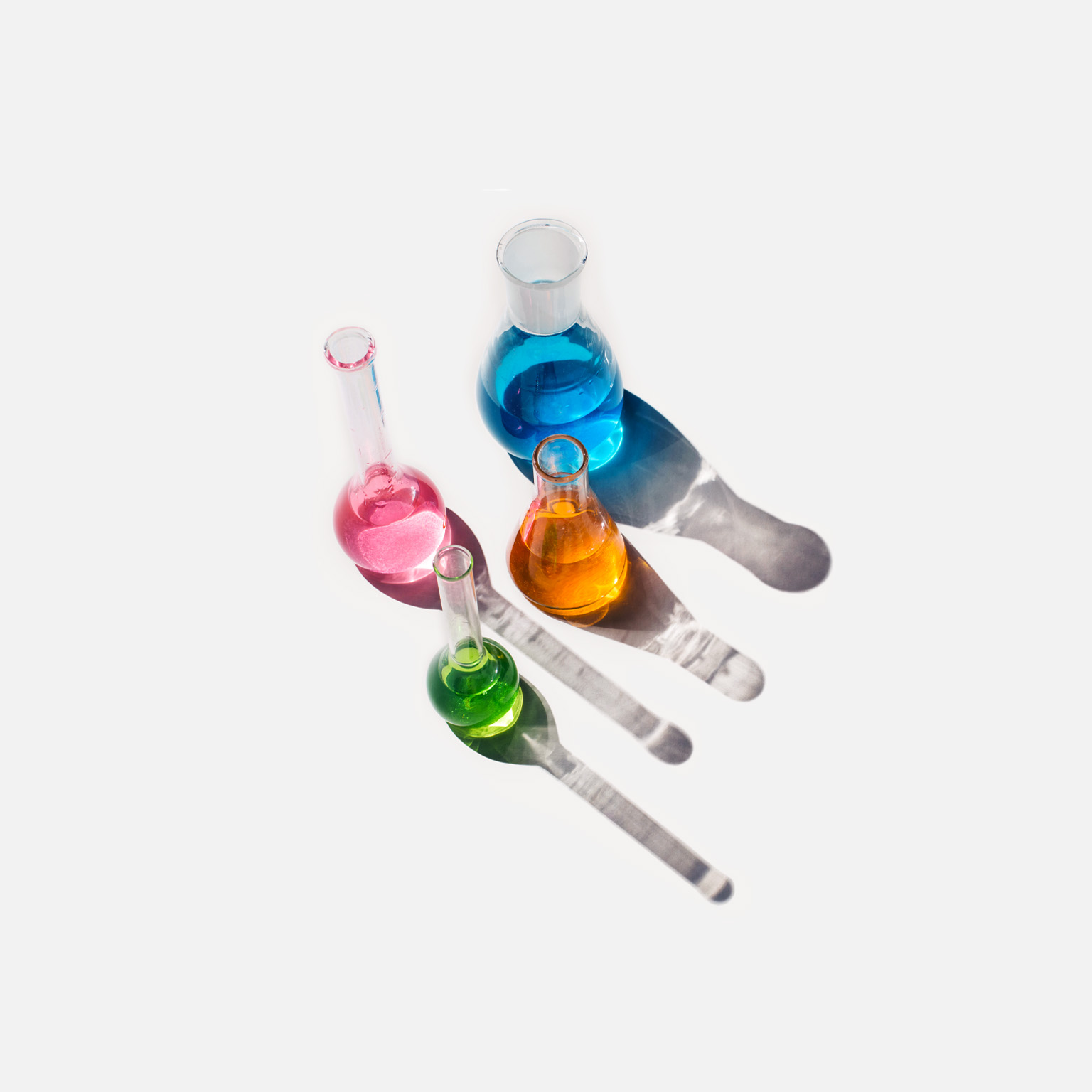 Laboratory glassware containing liquids of different colors on a light gray background. 