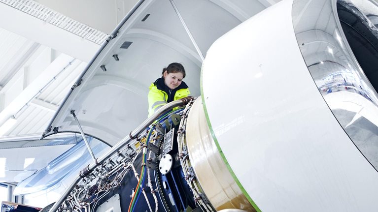 An engineer working on the engine of a commercial airliner in a large, airy hanger.