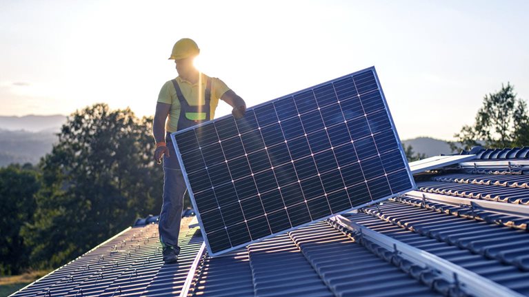 An image of a worker installing solar panels on the roof of a house.