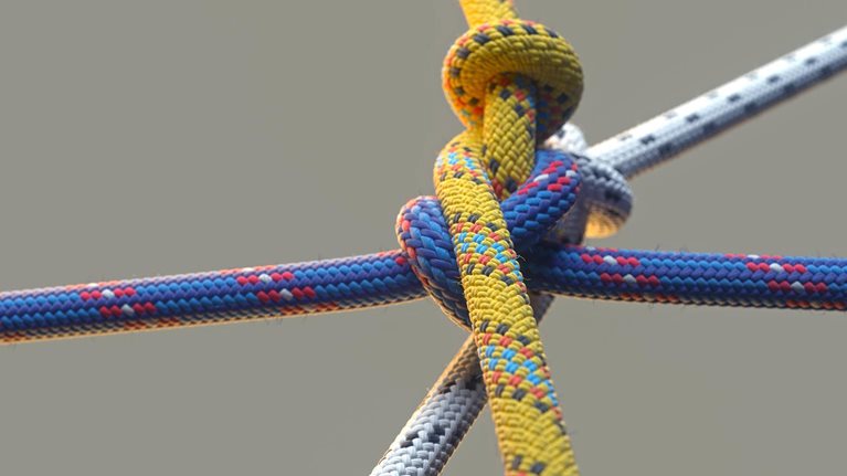 Close up image of three colored ropes knotting together on beige background.