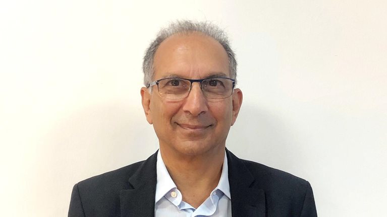 A smiling Homi Kharas photographed against a tan wall.