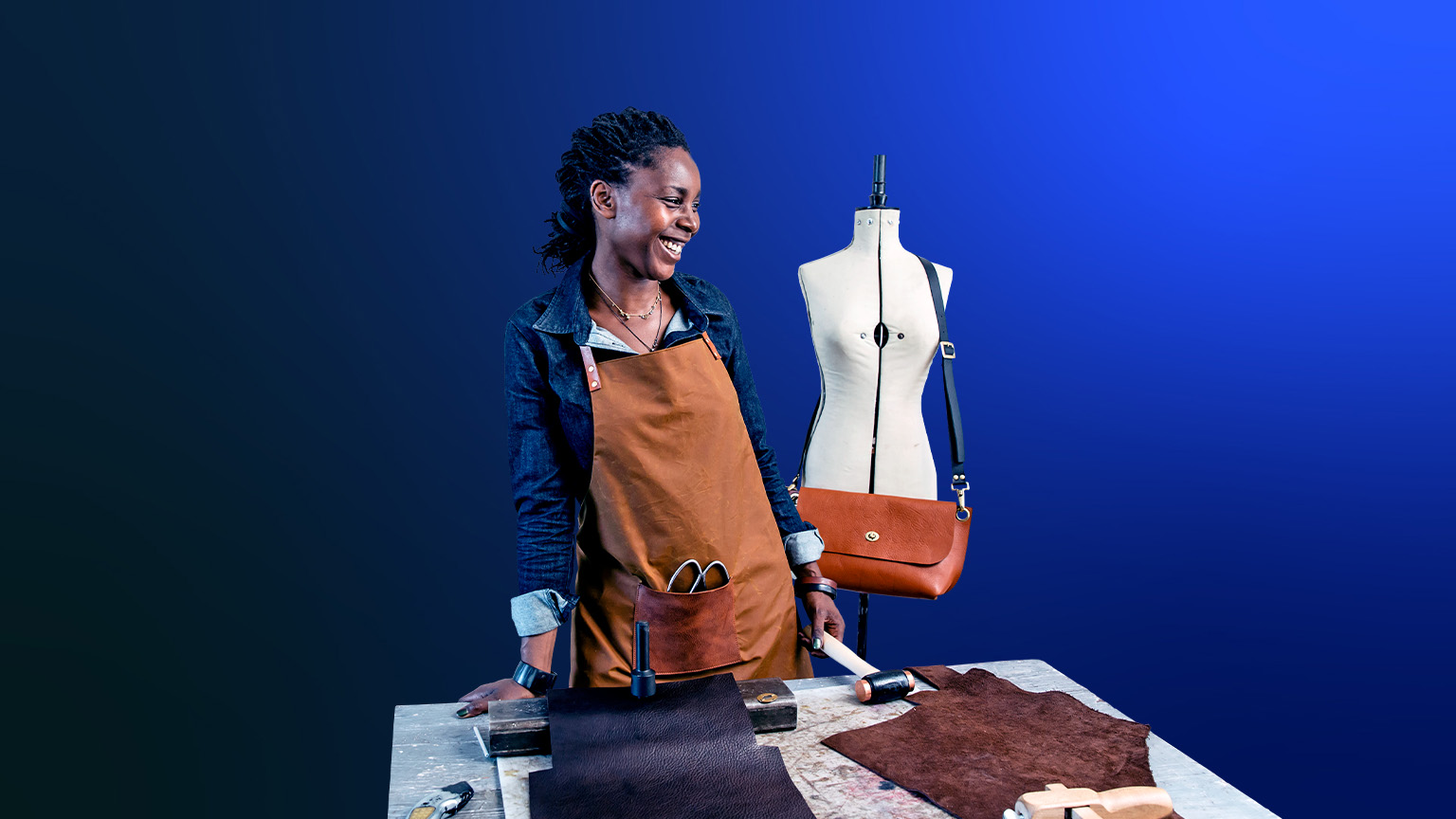 An image of a small business owner sharing a laugh at her design studio, where she makes leather goods to sell in her shop.