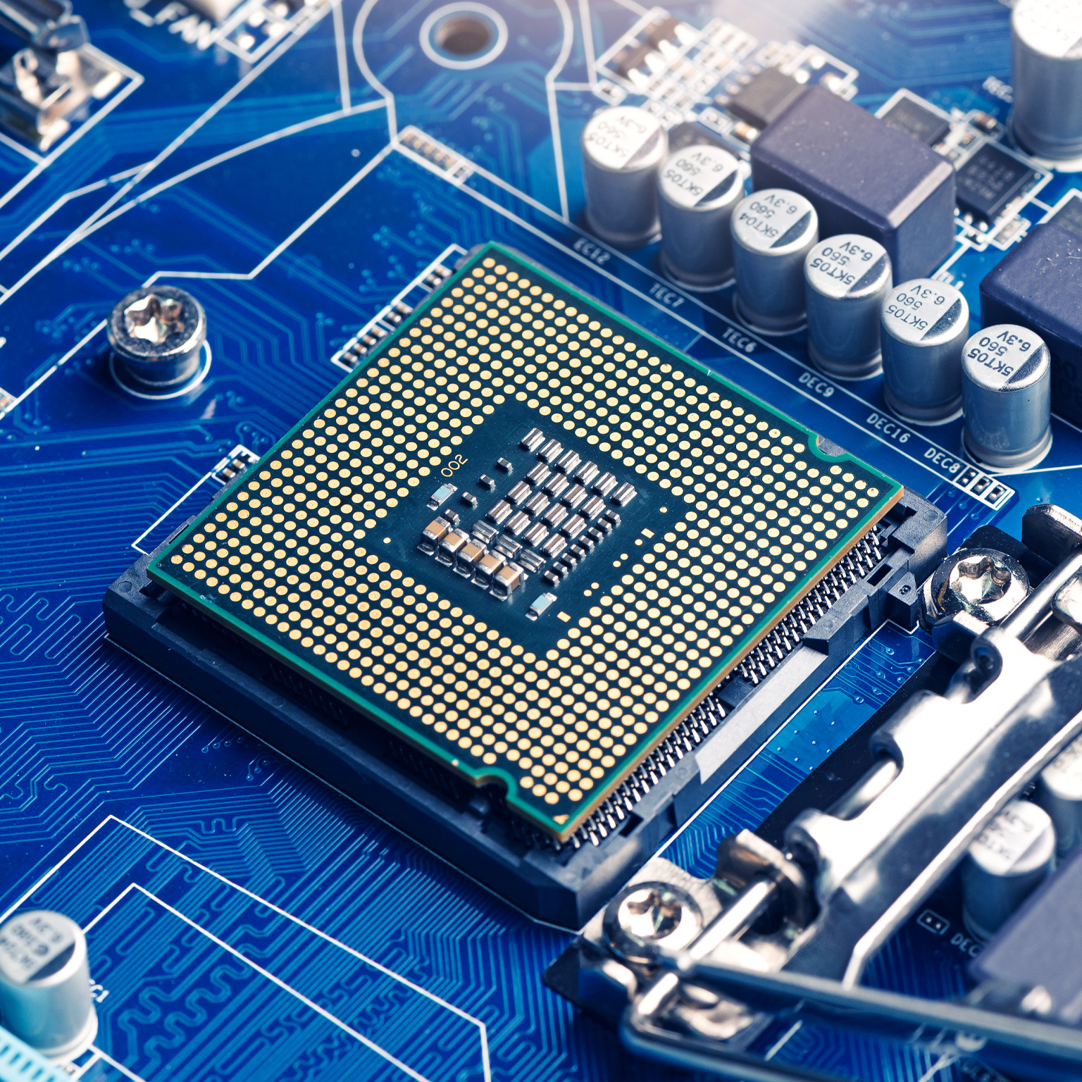 A close-up view of a computer processor mounted on a blue motherboard, surrounded by capacitors, circuits, and electronic components.