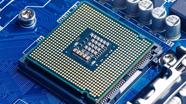A close-up view of a computer processor mounted on a blue motherboard, surrounded by capacitors, circuits, and electronic components.