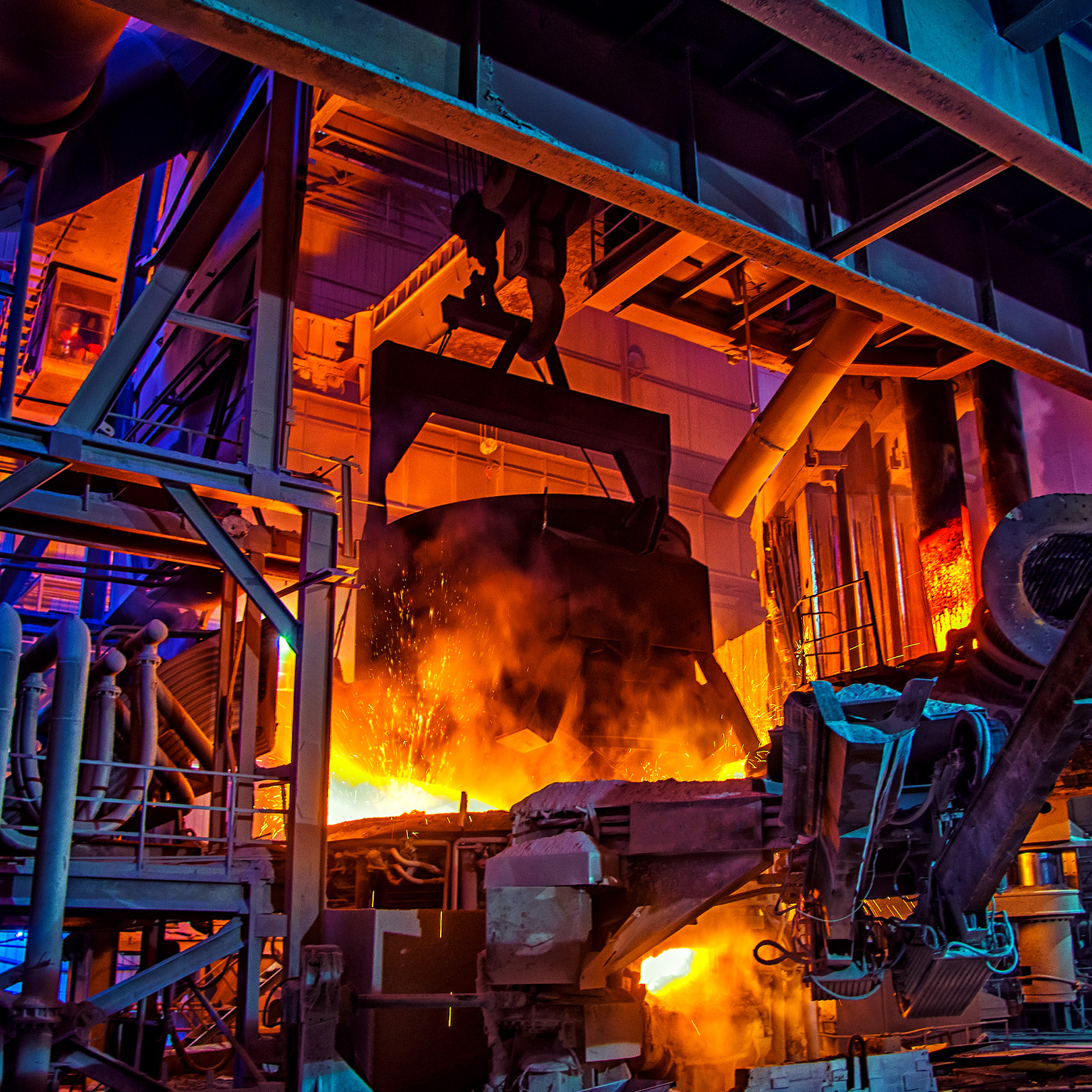 The interior of a large industrial steel plant, where molten metal glows bright orange amid heavy machinery and towering metal structures.