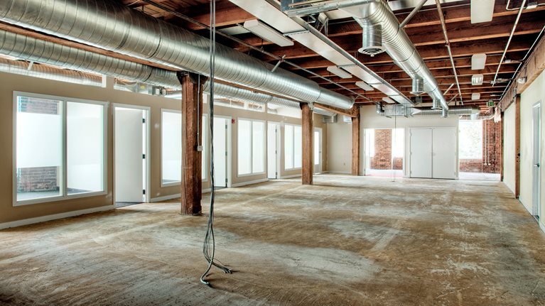 An empty office space with no furnishings or carpet and a bundle of wires hanging from the ceiling.